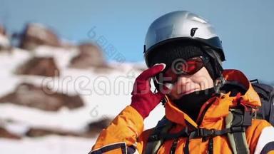 特写镜头，登山者戴着头盔和<strong>保暖夹克</strong>站在山上，用手固定眼镜